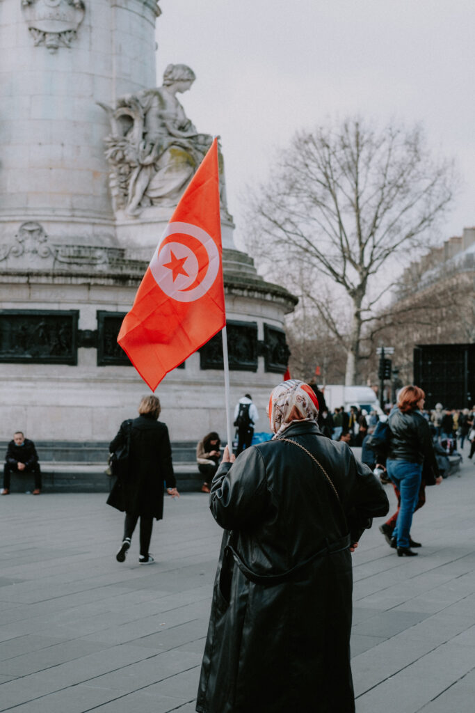 Place de la République à Paris, une femme de dos portant le voile, brandit un drapeau tunisien.
